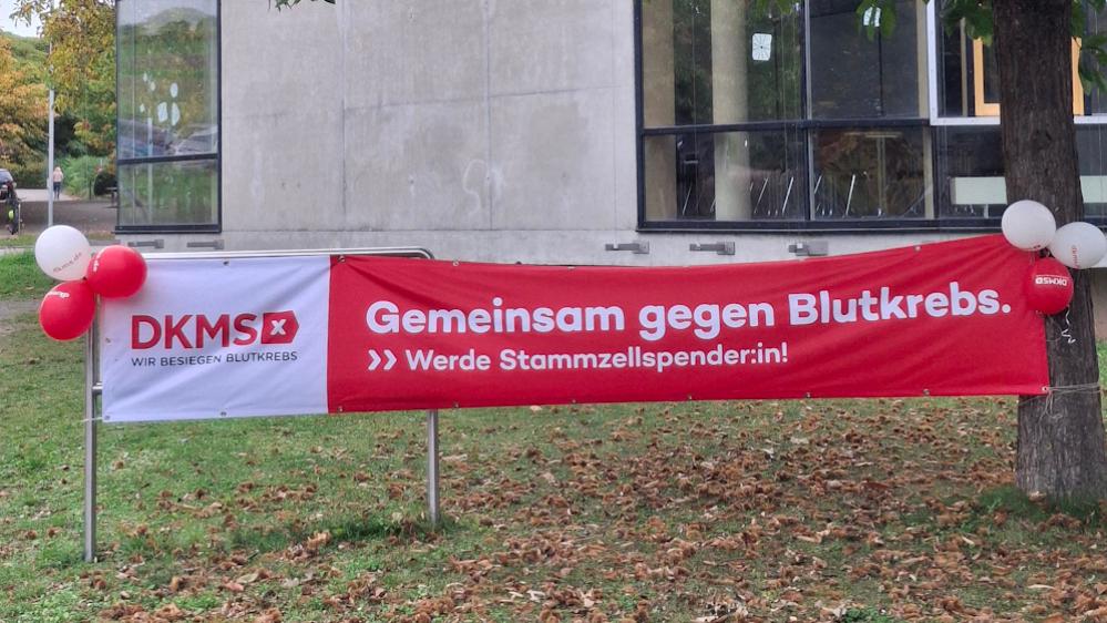 Ein rotes Banner mit der Aufschrift 'Gemeinsam gegen Blutkrebs' ist vor der Schule aufgespannt.